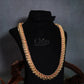 A thick gold-toned chain necklace embellished with red stones, displayed on a black velvet jewelry bust with decorative wood pieces in the background.
