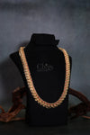 A thick gold-toned chain necklace embellished with red stones, displayed on a black velvet jewelry bust with decorative wood pieces in the background.