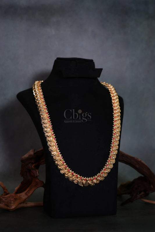 A thick gold-toned chain necklace embellished with red stones, displayed on a black velvet jewelry bust with decorative wood pieces in the background.
